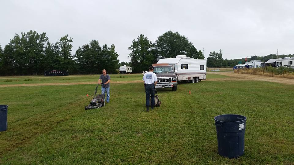 Ford F-Series truck towing an RV, two men mowing grass nearby