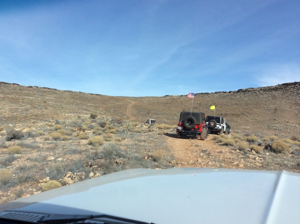 Three Jeep Wranglers driving off-road on a dirt trail in a desert landscape.