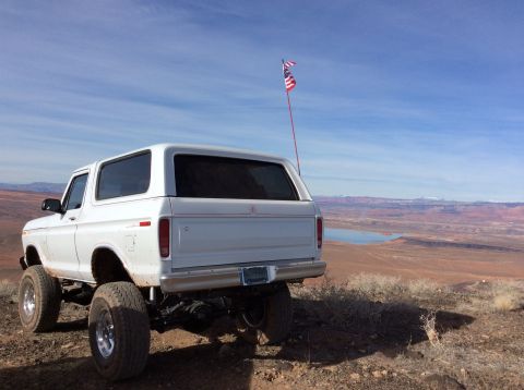 1979 Ford Bronco - A white, lifted 1979 Ford Bronco is parked on a dirt overlook, facing away from the camera, with a scenic desert landscape and a body of wa…