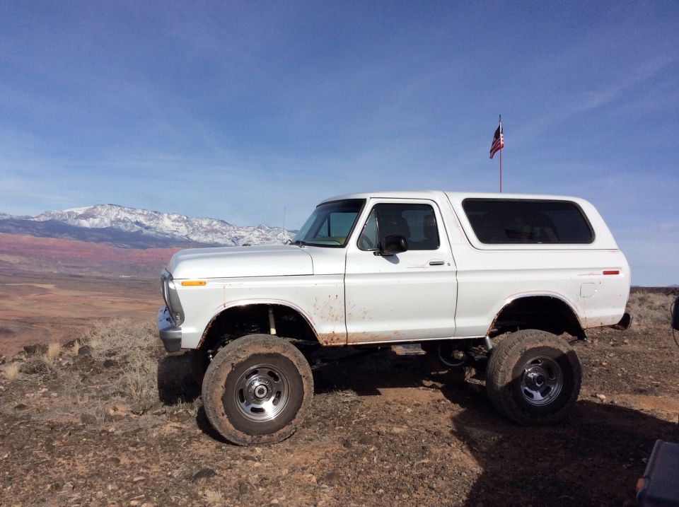 White lifted 1979 Ford Bronco parked on a dirt hill with mountains in the background.