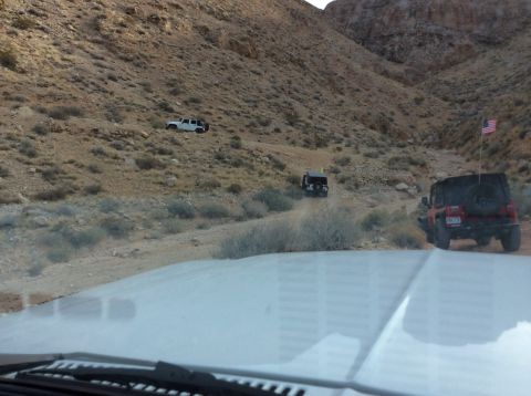 1979 Ford Bronco - A red Jeep Wrangler with an American flag on a pole is driving on a dirt road in a rocky, mountainous desert landscape. Another Jeep is vis…