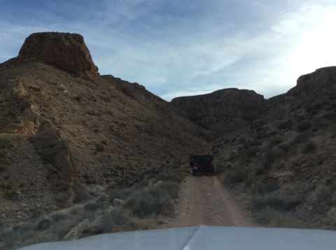 1979 Ford Bronco - A dark-colored Jeep Wrangler is driving on a dirt road through a rocky canyon. The vehicle is seen from the rear as it travels away from th…