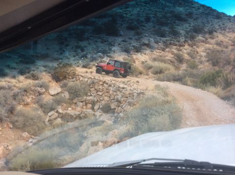 1979 Ford Bronco - A red Jeep Wrangler is parked on a dirt road next to a stone wall on a rocky hillside.