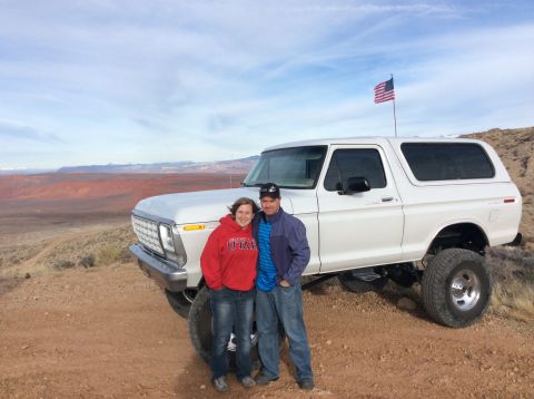 1979 Ford Bronco - A couple poses in front of a lifted white 1979 Ford Bronco with an American flag flying from a pole on the roof. The vehicle is parked on a…