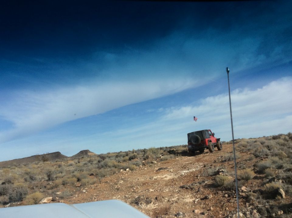 Red Jeep Wrangler driving on a desert road with an American flag.
