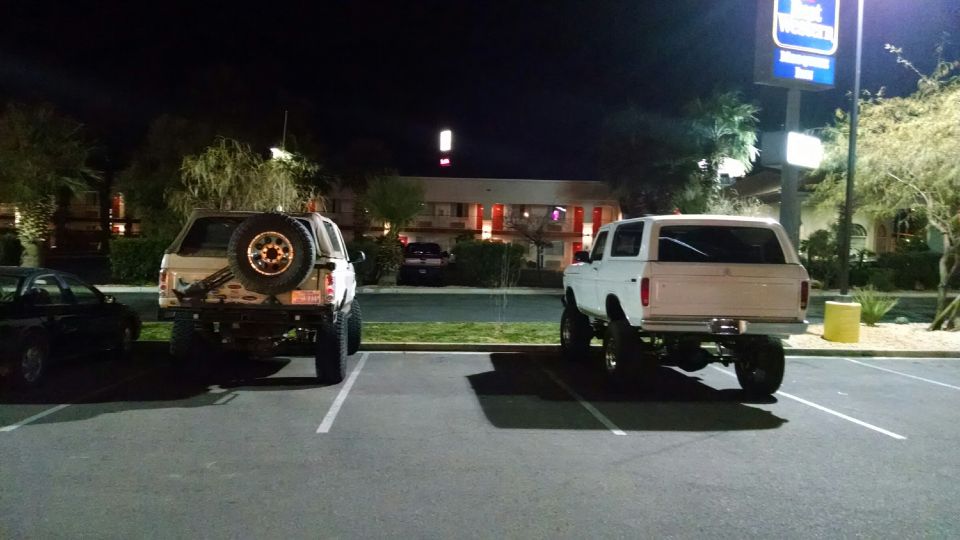 Two lifted SUVs parked at night in front of a motel.