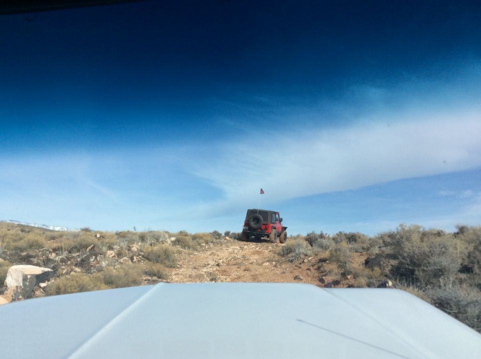Red Jeep Wrangler on a rocky hillside with an American flag.