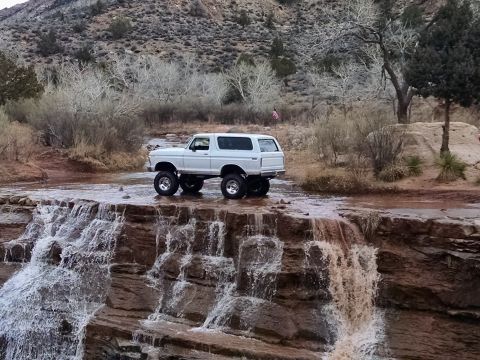 1979 Ford Bronco - A white 1979 Ford Bronco is parked on the edge of a waterfall in a rocky, arid landscape.