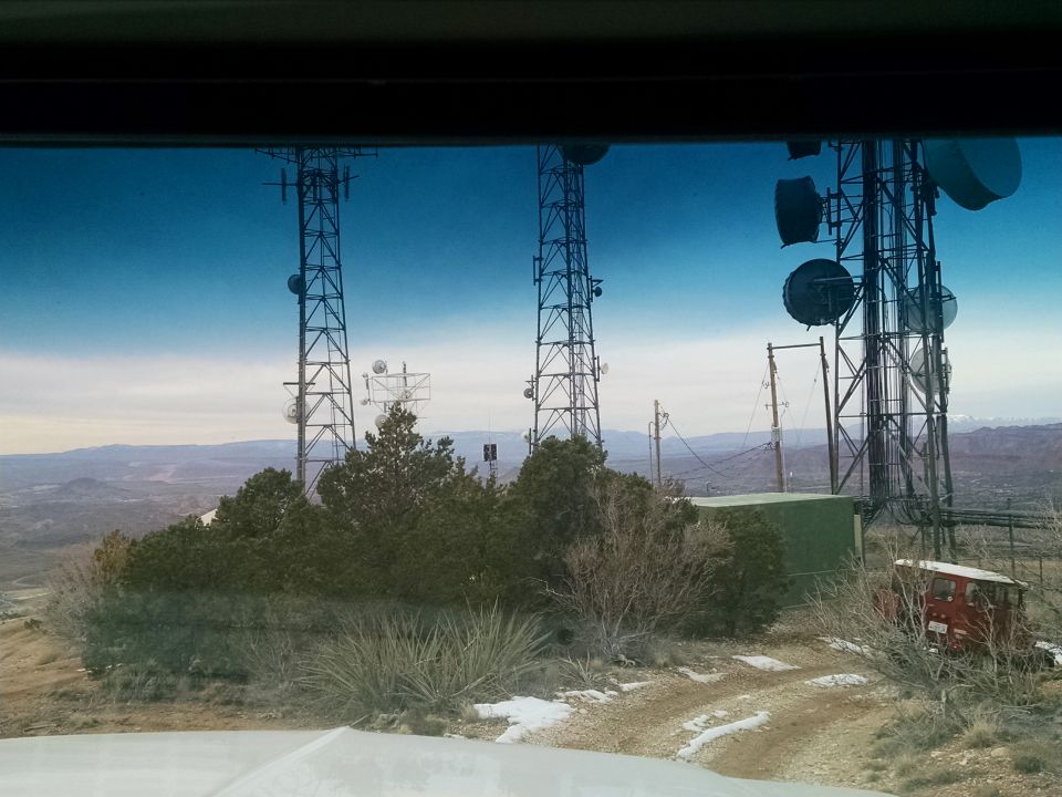 Red vintage SUV parked on a dirt road with communication towers in the background.