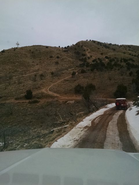 1979 Ford Bronco - A red vintage SUV, likely a Ford Bronco, drives on a dirt road with patches of snow. The vehicle is heading up a winding mountain road towa…