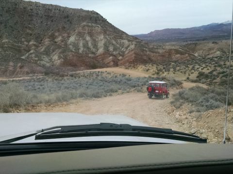 1979 Ford Bronco - A red vintage SUV drives on a dirt road through a desert landscape with mountains in the background. The photo is taken from inside another…