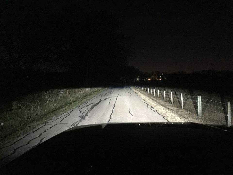 View from inside a vehicle driving on a road at night, showing headlights illuminating the road ahead.