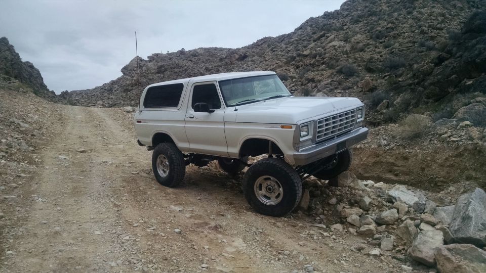 Lifted white 1979 Ford Bronco on a rocky off-road trail.