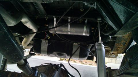 1979 Ford Bronco - Underside view of a vehicle showing the exhaust system, a fuel tank, and an air tank mounted above it. A shock absorber and leaf springs ar…