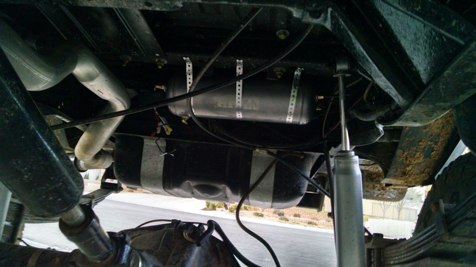Underside of a vehicle showing exhaust, fuel tank, air tank, shock, and leaf springs.