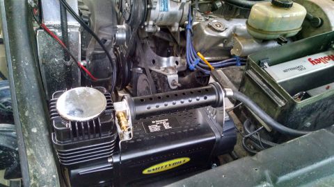 1979 Ford Bronco - A black Smittybilt air compressor is mounted in the engine bay of a vehicle, next to the radiator and engine components. The compressor has…
