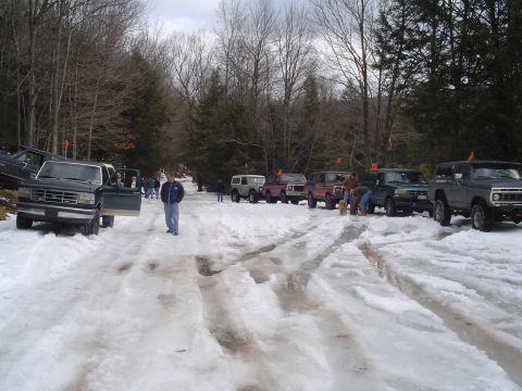 1993 Ford Bronco - A group of SUVs are parked on a snow-covered road in a wooded area, with one vehicle's door open.