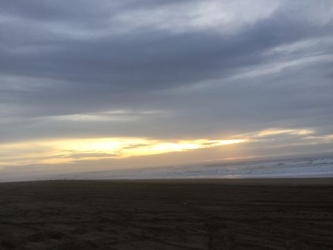 1989 Ford Bronco - A beach scene with tire tracks imprinted in the sand, under a dramatic sky as the sun sets over the ocean.