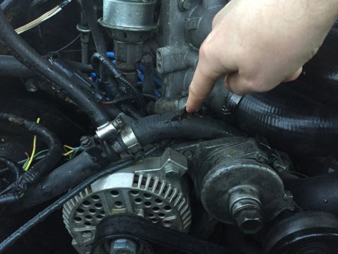 1989 Ford Bronco - A close-up view of a damaged engine hose with a finger indicating the tear.