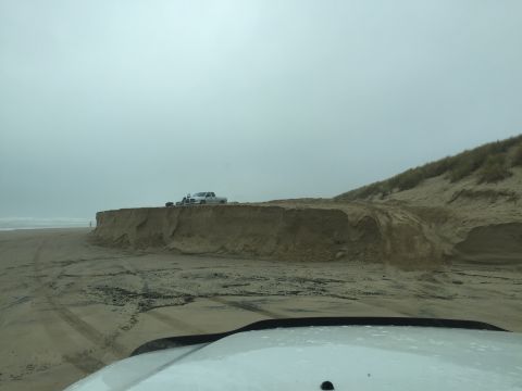 1989 Ford Bronco - A white pickup truck is parked on a sandy cliff overlooking the beach and ocean on a cloudy day.