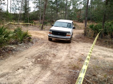 1992 Ford Bronco - White 1992 Ford Bronco navigates a sandy, wooded trail, with caution tape visible.