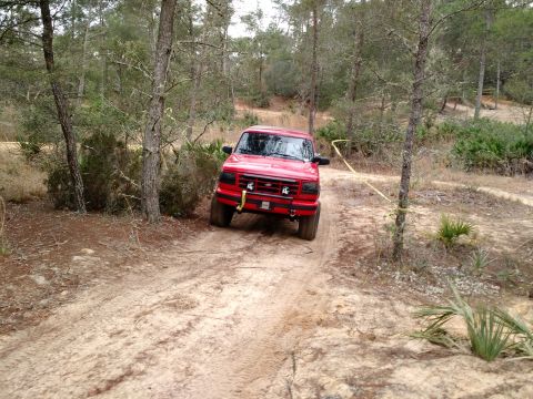 1992 Ford Bronco - A red Ford F-150 navigates a sandy trail through a wooded landscape.