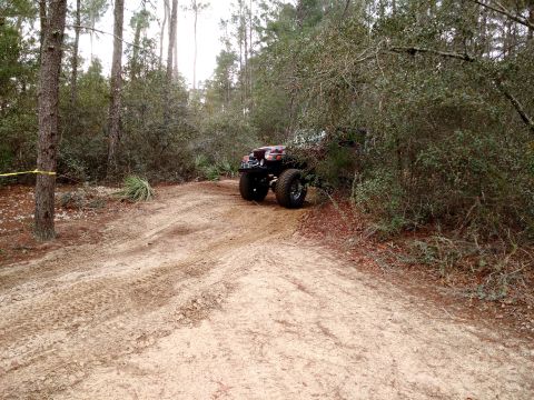 1992 Ford Bronco - An off-road vehicle navigates a sandy trail surrounded by trees and brush.
