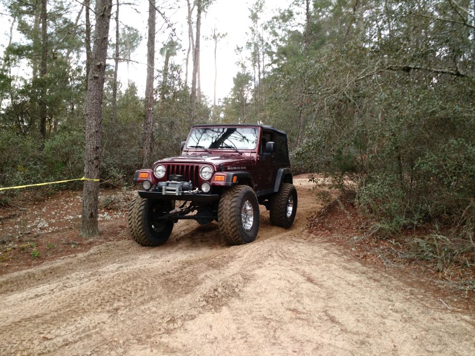 Maroon Jeep Wrangler Rubicon with lifted suspension on a sandy trail