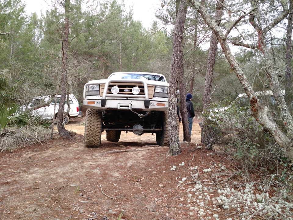 1992 Ford Bronco with large tires and bull bar parked off-road, another white SUV visible behind it