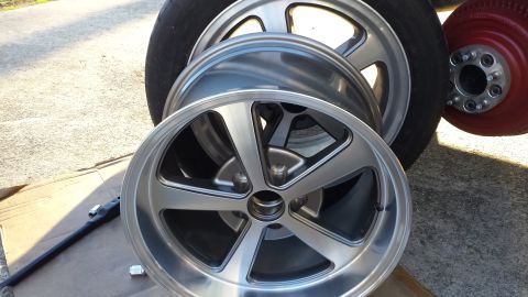 1976 Ford Ranchero - A collection of alloy wheels, including one with a red painted rim, are displayed outdoors.