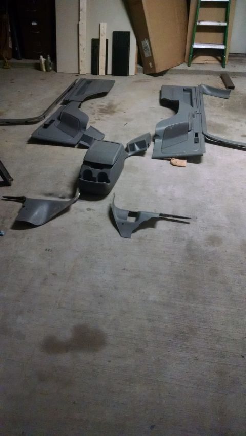 1995 Ford Bronco - Various interior car parts are disassembled and spread across a concrete floor in what appears to be a garage or workshop.