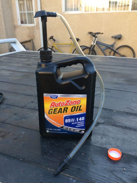 1987 Suzuki Samurai - A bottle of AutoZone Gear Oil with a pump and hose is placed on a wooden surface, with two bicycles visible in the background.
