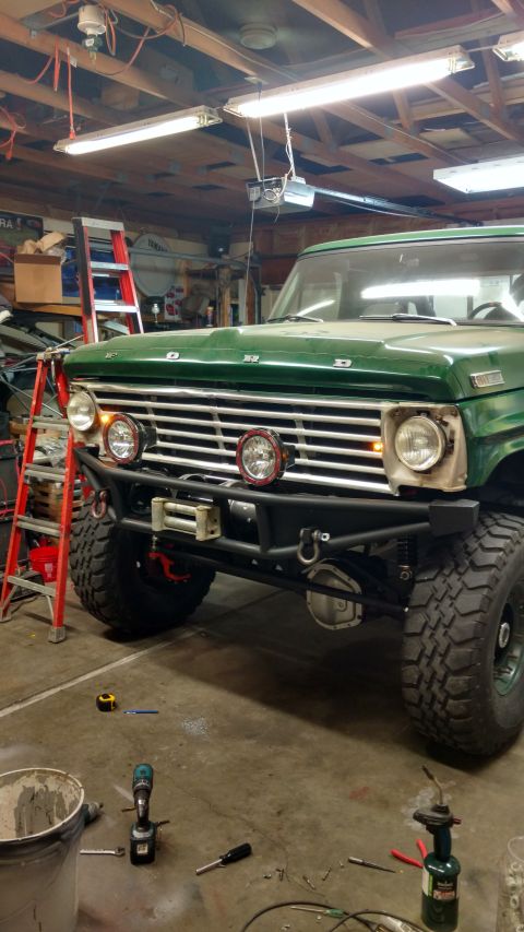 1967 Ford F-250 - A green 1967 Ford F-250 is parked in a garage, showing its front end with a custom bumper and winch.