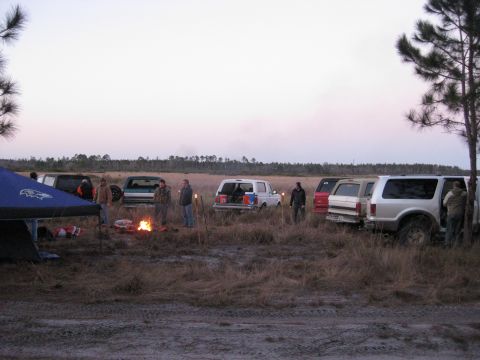 1994 Ford Bronco - Several SUVs, including a 1994 Ford Bronco, are parked in a field as people gather around a campfire at dusk.