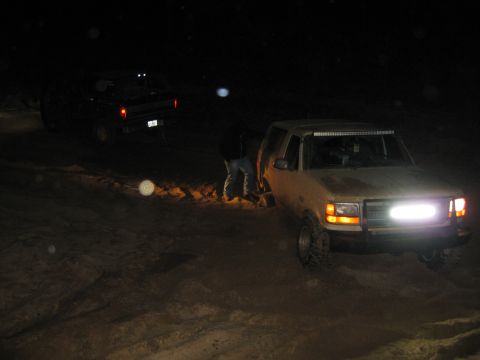 1994 Ford Bronco - Two trucks are off-roading at night, one with a light bar and front light.