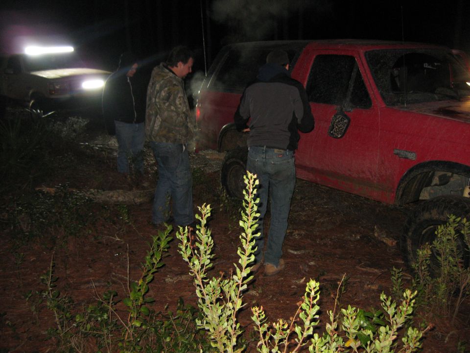 Red 1994 Ford Bronco parked at night with people nearby