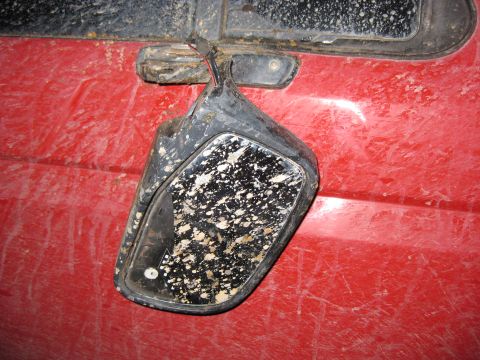 1994 Ford Bronco - Mud-splattered side mirror hanging from a red vehicle door.