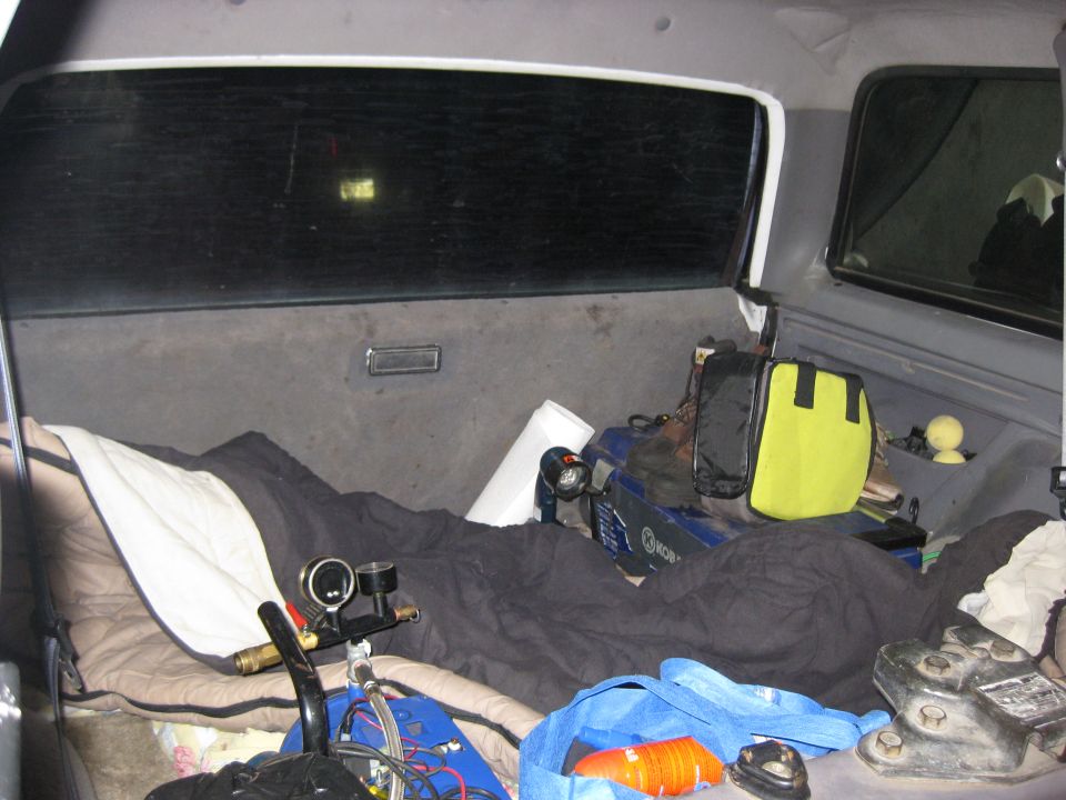 Interior view of a vehicle's cargo area with sleeping bags, camping gear, and a blue tote bag