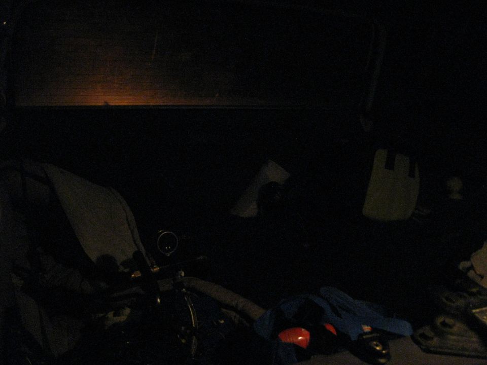 View from inside a dark vehicle, showing a steering wheel, dashboard, and some items in the back seat. A faint light is visible through the windshield