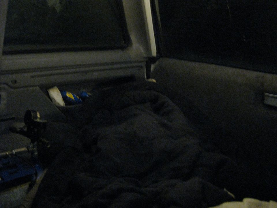 Interior of a dark vehicle with a blanket covering the seats and a blue tool bag on the floor