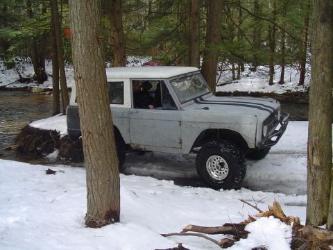 1993 Ford Bronco - A classic Ford Bronco navigates a snowy, wooded area with a stream nearby.