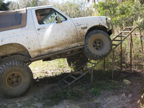 1994 Ford Bronco - A white Ford Bronco with a tan soft top navigates a metal ramp, covered in mud.