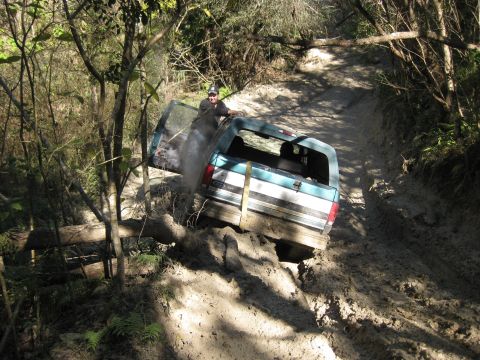 1994 Ford Bronco - A driver navigates a muddy off-road trail with a Ford Bronco, its door ajar.