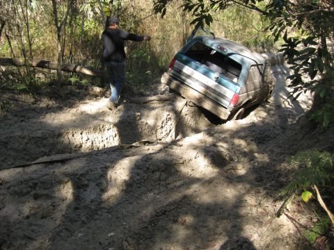 1994 Ford Bronco - A teal and white 1994 Ford Bronco is stuck in a muddy off-road trail, with a person standing nearby.