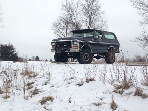 1979 Ford Bronco - Lifted black Ford Bronco sits in a snowy landscape with bare trees in the background.