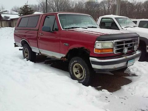 1990 Ford Bronco - This red Ford F-150 pickup truck with a camper shell is parked in the snow next to another truck.