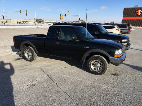 Black Ford Ranger pickup truck parked in a lot, other vehicles and a building in background