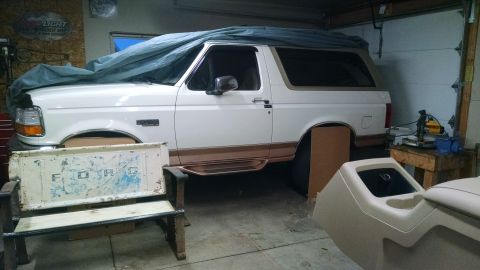 1994 Ford Bronco - A white Ford Bronco is partially covered by a tarp in a garage, with a bench made from a Ford tailgate nearby.