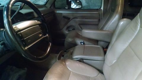 1994 Ford Bronco - The interior of a vehicle, tan leather seats and a prominent steering wheel, is captured in this image.