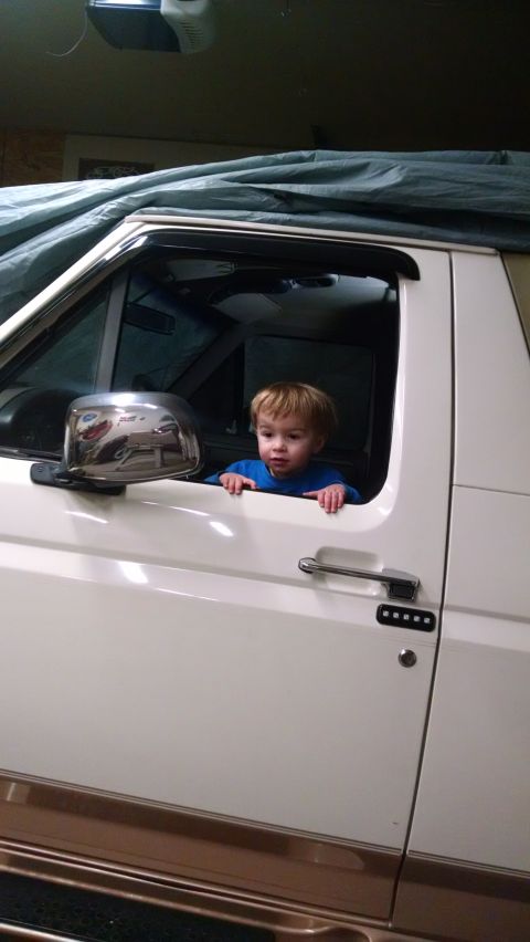 1994 Ford Bronco - A young child looks out from the driver's seat of a white Ford Bronco, which is covered by a tarp.